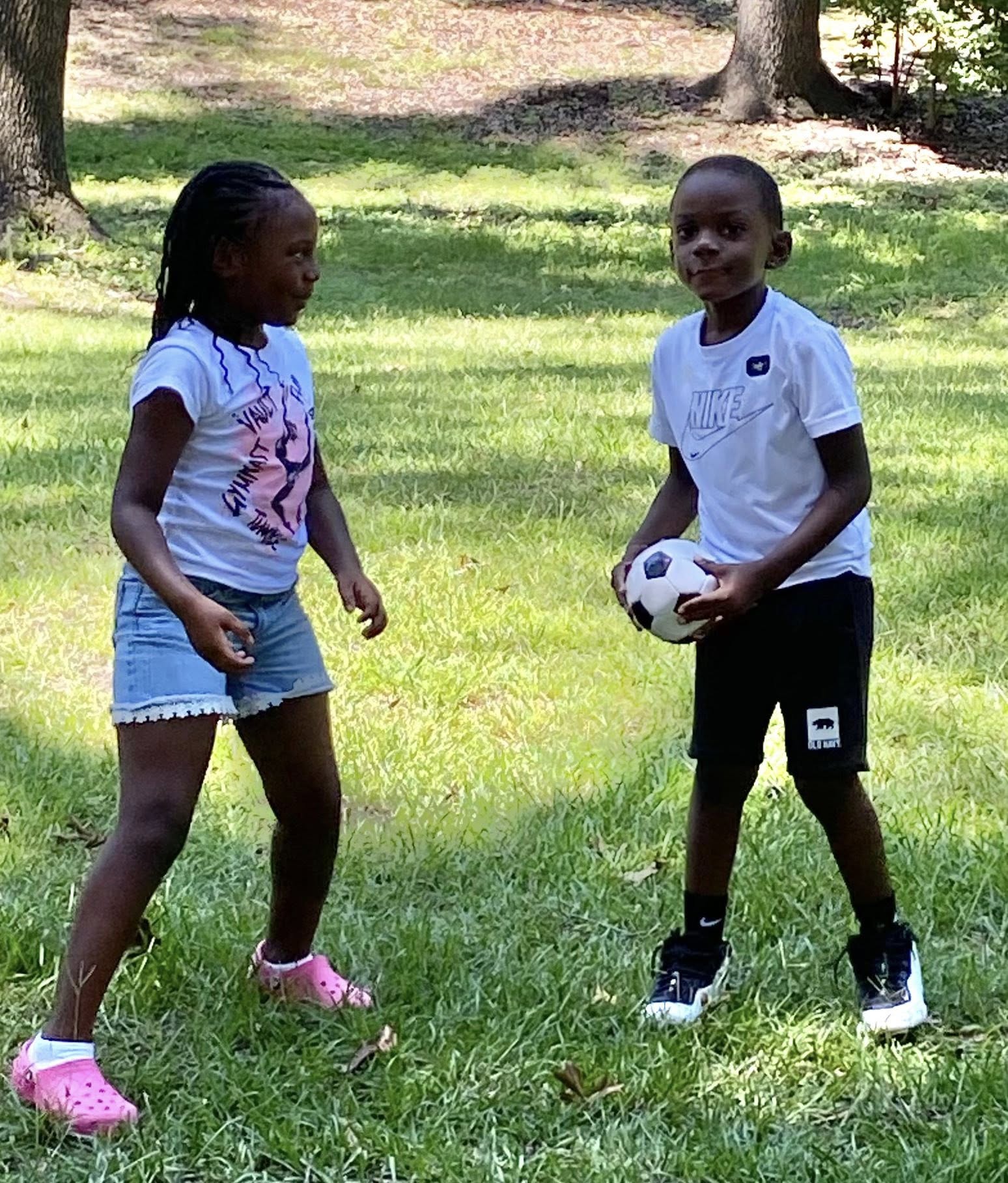  A little girl and a little boy playing with a small soccer ball.